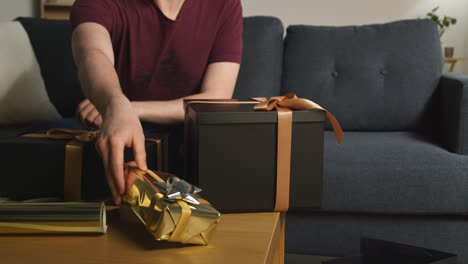 Close-Up-Of-Man-Gift-Wrapping-Presents-On-Table-At-Home-With-Wrapping-Paper-Sticky-Tape-And-Scissors